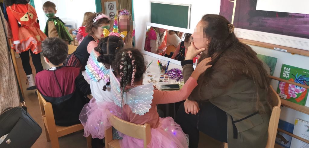 Fasching im Familienzentrum Fennpfuhl, Kinder und 1 Erwachsener sitzen am Tisch mit Schminckzeug
