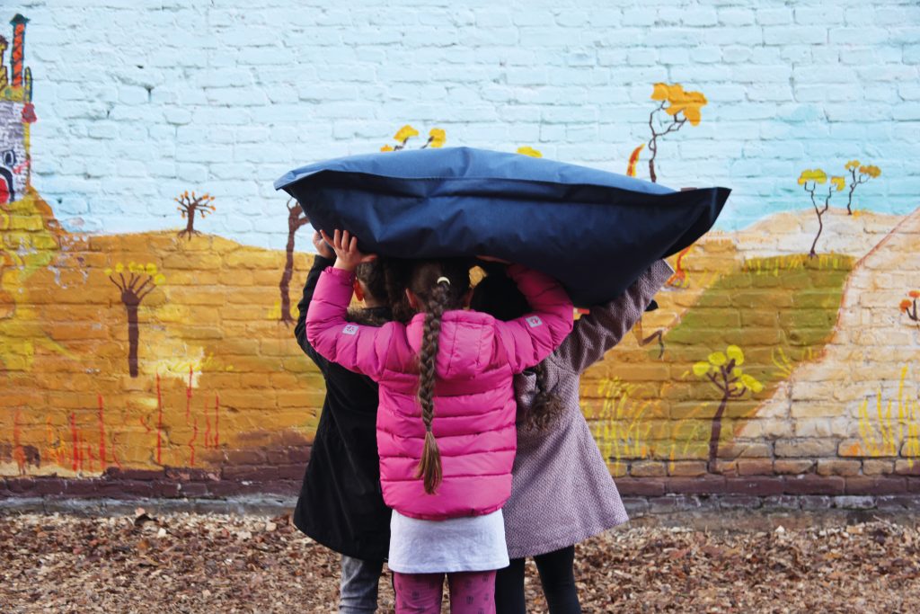 Kind mit großem Spielkissen auf dem Kopf von hinten zu sehen