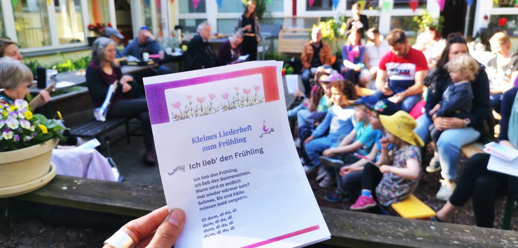AWO FAZ Fennnpfuhl, Frühlingsfest 2025, Singegruppe im Hintergrund und hand mit einem Liedtetxt im Vordergrund