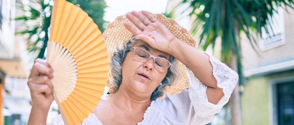 Bild: AdobeStock_©Krakenimages_älterer Frau mit Fächer an heißem Tag wischt den Schweiß von der Stirm