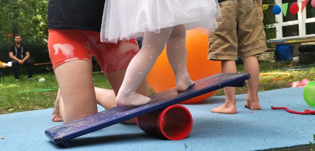 FAZ Fennpfuhl-Zirkusnachmittag, kleine Kinderfuesse balancieren mit Hilfe eines anderen kindes auf der Rolle mit einem Brett