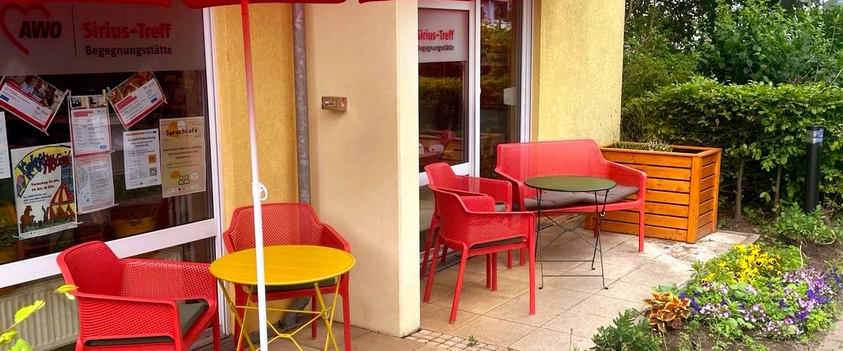 AWO Siriustreff Terasse mit roten Stühlen und gelben Tischen, Blumenbeet davordavor